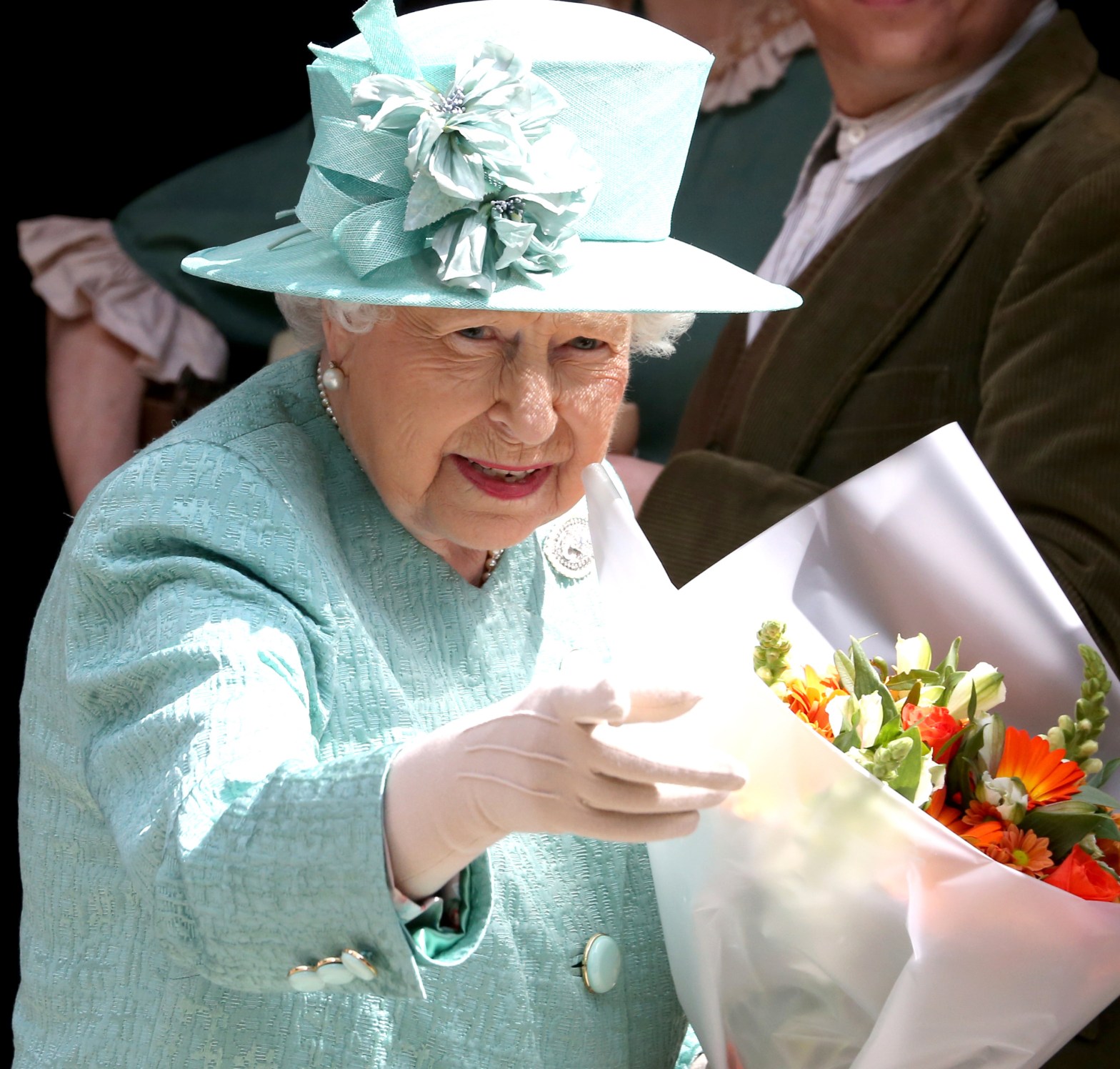 Queen Elizabeth II in turquoise jacket and hat, with a bouquet of flowers.